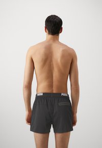 Håndballshorts for menn i mørkegrå med elastisk midje, en hvit logo og en liten baklomme med glidelås. Glatt tekstur.
