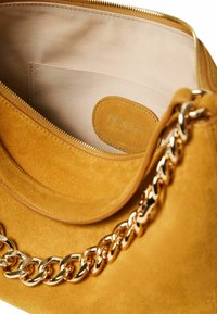 Borsa in suede gialla senape con tracolla in catena dorata. Presenta una chiusura con zip e un interno in tessuto beige con un'etichetta del logo.