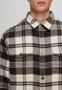 Brown and cream plaid shirt jacket, made of thick fabric, featuring two chest pockets, button closure, and a pointed collar.