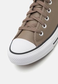 Bruna lädersneakers med vit gummikappa, bruna skosnören, metallöglor och vit texturerad sula med svart rand.