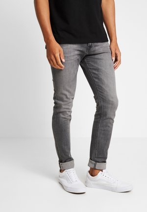 Cienkie szare dżinsy o wyblakłym wykończeniu, z podwiniętymi mankietami i pięcioma kieszeniami, zestawione z białymi trampkami i czarnym t-shirtem.