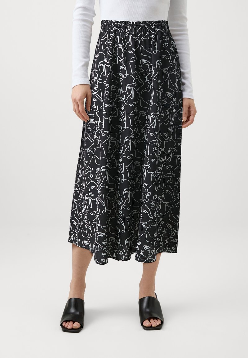 Jupe midi noire avec motifs abstraits en lignes continues blanches représentant des visages, taille élastique, portée avec un haut blanc à manches longues et des chaussures noires à bout ouvert.