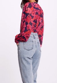 Blusa semi transparente de manga larga con un fondo azul marino oscuro y un gran estampado de flores rosas, combinada con jeans de mezclilla celeste de cintura alta.