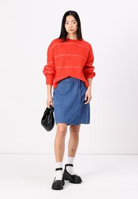 Red striped knit sweater with wide sleeves, denim pencil skirt, black handbag, white socks, and chunky black shoes. Model stands against a plain background.