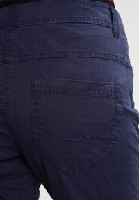 Námořnické modré bavlněné šortky s designem zadní kapsy, která má zakřivený steh. Jemná textura a lehká tkanina jsou patrné.