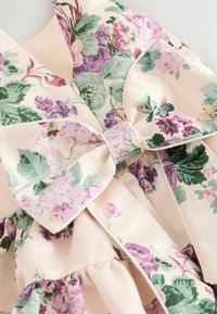 Ziedu auduma kleita ar lielu loku detaļu, krāsota ar rozā, violetes un zaļas krāsas ziediem uz gaiša krēmveida fona.