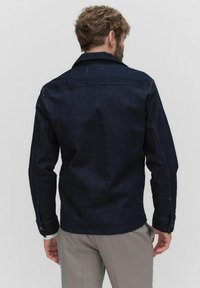 Mörkblå denimjacka med knäppta manschetter, klassisk krage och synliga sömnadsdetaljer. Bakdelen har en skräddarsydd passform och minimalistisk design.