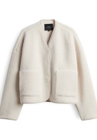 Giacca in pelliccia ecologica color crema chiaro, con silhouette rilassata, maniche larghe e due grandi tasche frontali. Senza chiusure né colletto.