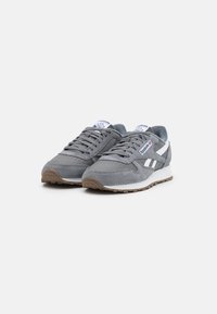 Zapatillas de ante gris con acentos blancos, que cuentan con una parte superior texturizada, cierre de cordones y una suela de goma con un dibujo en relieve.