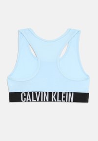 Lyseblå sportsbh med racerback-design, med en svart kant med "CALVIN KLEIN" i hvit skrift. Myk bomullsmateriale.