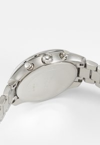 Relógio cronógrafo em aço inoxidável com um acabamento prateado polido, três botões e uma coroa texturizada. Apresenta um fundo sólido sem gravações.