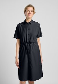Zwarte shirtjurk met korte mouwen, knopen aan de voorkant en een drawstring taille. Glad textuur en knielengte met zijsplitten.
