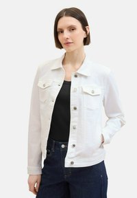 White denim jacket with a pointed collar, front snap buttons, two chest pockets, and a straight fit. Worn over a black top and blue jeans.