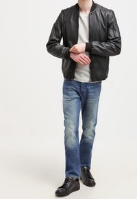 Giubbotto bomber in pelle nera con polsini a coste, t-shirt grigia a collo rotondo, jeans azzurri chiari e sneakers nere. Design semplice, look informale.