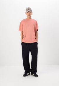 Jasnoróżowa koszulka z krótkim rękawem, w zestawie z czarnymi spodniami dresowymi z elastycznym pasem i bocznymi kieszeniami, uzupełniona szarym czapką.