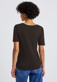 Tmavě hnědé tričko s krátkým rukávem, širokým výstřihem a mírně přiléhavým střihem, spárované se světle modrými džíny.