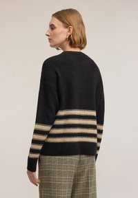 Maglione nero a maglia con righe orizzontali crema e nere, con finitura testurizzata e vestibilità comoda, abbinato a pantaloni a quadri.