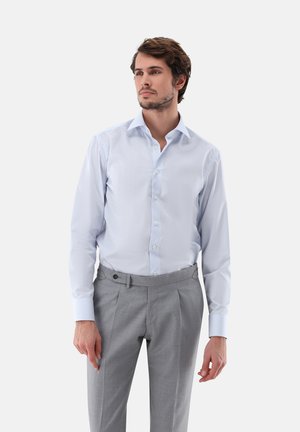 Helles blaues Hemd mit Kragen, Knopfleiste und langen Ärmeln, kombiniert mit grauen Hosen mit flachem Vorderteil und seitlichen Taschen.