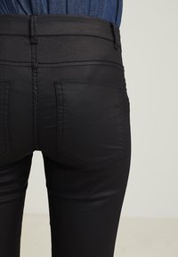 Černé skinny džíny s hladkou texturou, se středně vysokým pasem, dvěma zadními kapsami a detailním prošíváním podél švů.