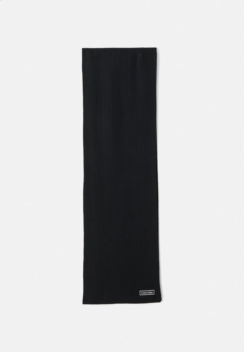 Zwarte geribbelde gebreide sjaal met een klein rechthoekig Calvin Klein-logo-label dichtbij een van de uiteinden op een witte achtergrond.