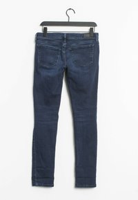 Jeans skinny de mezclilla de color azul oscuro colgados en una percha negra, con un diseño estándar de cinco bolsillos y detalles de costura mínimos en la parte trasera.