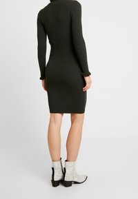 Mörkgrön ribbad stickad klänning med långa ärmar och volangärmar, matchad med vita och grå ormskinsmönstrade ankelboots med svarta detaljer.