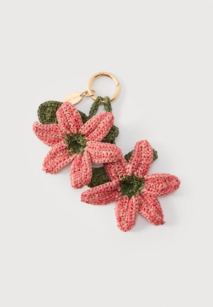 Schlüsselanhänger mit zwei pinkfarbenen, gehäkelten Blumen mit grünen Zentren und Blättern, befestigt an einem goldenen Ring mit einer kleinen ovalen Anhängermarke.