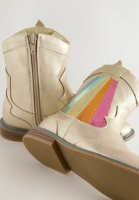 Botas metálicas doradas hasta el tobillo con cremallera lateral, que presentan un diseño colorido de arcoíris en varios tonos pastel y un acento de estrella.