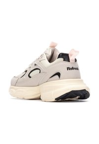 Zapatilla deportiva beige con detalles en negro y rosa. Presenta una suela acolchada, parte superior texturizada y un diseño distintivo con recortes.