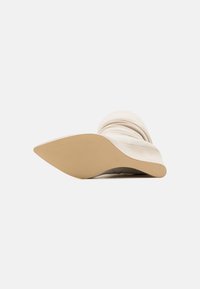 Botte de cheville en tissu beige avec un bout pointu et une texture froissée, dotée d'une semelle extérieure en caoutchouc beige avec des motifs de grip texturés.