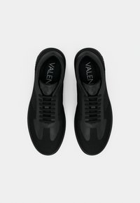 Ζευγάρι μαύρα δερμάτινα και υφασμάτινα αθλητικά παπούτσια με μαύρα κορδόνια, στρογγυλεμένες μύτες και την επιγραφή "VALEN" ορατή στις εσωτερικές σόλες, φαίνονται από ψηλά.