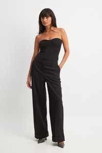 Svart strapless bodysuit kombinerad med högmidjade, vida svarta byxor. Byxorna har en slät yta och uppvikta fållar.