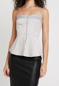 Ljust grå peplumtop med justerbara spaghetti-axelremmar och en rad med tryckknapps-stängningar framtill, kombinerad med en svart läderskjort.