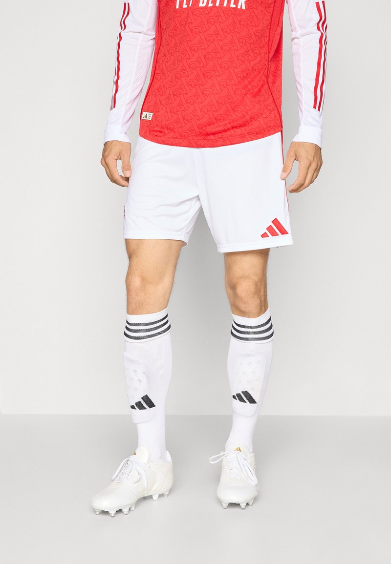 Rød fodboldtrøje med hvide ærmer og mønsterdesignet, parret med hvide shorts, hvide sokker med sorte striber og hvide støvler.