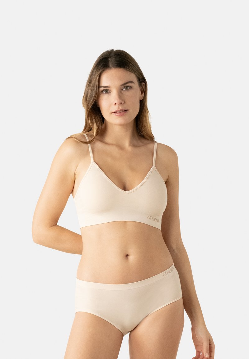 Bralette beige clair avec un décolleté en V et des bretelles ajustables, associée à un slip assorti arborant un logo discret sur la ceinture.