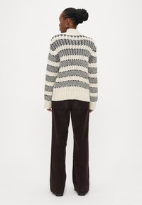 Pletený svetr s černými a krémovými pruhy, žebrovanou strukturou a kulat�ým výstřihem, kombinovaný s hnědými manšestráky s rozšířenými nohavicemi.