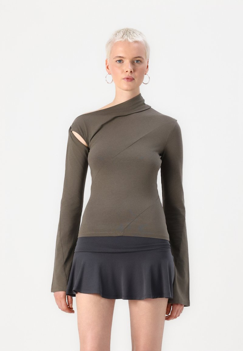 Asymmetrisch olijfgroen top met lange mouwen en een uitsnijdetail; gecombineerd met een donkersgrijze flared minirok. Zachte textuur.