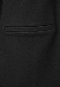 Närbild av ett svart tygplagg med en horisontell passpo pockets. Tyget har en fin, tät stickad struktur.