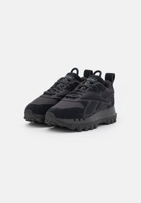 Chaussures de sport noires avec une tige en matériau mixte, comprenant du mesh et du daim. Semelle à crampons épaisse et doubles languettes de traction au talon.