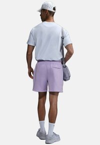 Camiseta gris claro, pantalones cortos lila con cintura elástica y zapatillas grises. Diseño sencillo con un bolso de hombro y calcetines blancos.