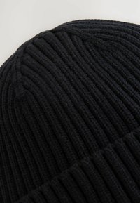 Berretto lavorato a maglia nero con texture a coste verticali, dotato di una parte superiore arrotondata e di una fascia spessa. Il materiale sembra morbido e caldo.