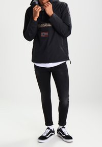 Felpa leggera nera con cappuccio, con logo e toppa della bandiera norvegese. Indossata con jeans neri e sneakers nere e bianche.