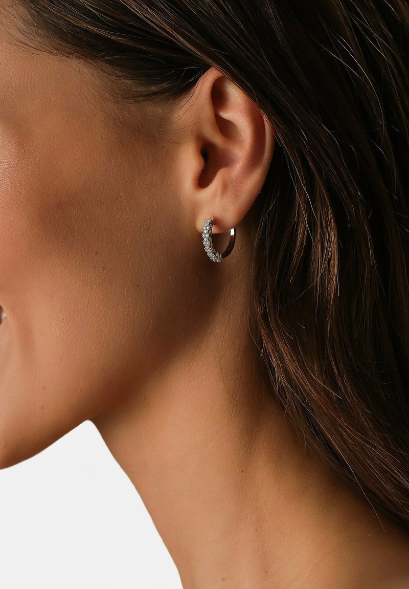 Silberne Creolen mit einem geschwungenen Design, die entlang der Vorderkante kleine klare Steine und eine polierte Oberfläche aufweisen.