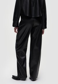 Zwarte leren broek met een losse pasvorm, voorzien van een gladde textuur en wijde pijpen. Gecombineerd met zwarte hakken voor een samenhangende uitstraling.