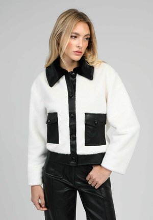 Veste courte en fausse fourrure blanche avec devant en faux cuir noir, boutons noirs et deux poches avant avec rabats. Texture douce, coupe décontractée.