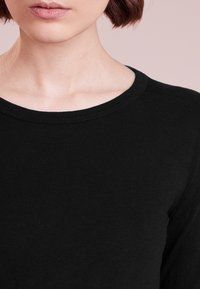 Musta pitkähihainen paita, jossa on pyöreä pääntiellä. Silkkinen pinta ja vähäiset ompelusaumat kaula-aukossa. Yksinkertainen, tasavärinen muotoilu.