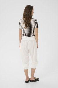 Svartvitrandig kortärmad topp, vita elastiska midje löst sittande byxor, svarta slip-on skor med dekorativa hårdvaruaccents.