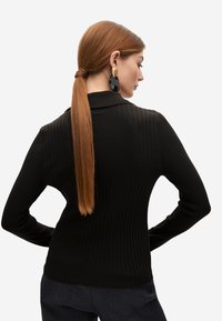 Jersey negro de canalé con cuello de solapa y mangas largas, que presenta una textura en la tela y una silueta ajustada.