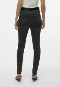 Jeans skinny de tiro alto en negro, hechos de denim, con dos bolsillos traseros, silueta ajustada y dobladillos deshilachados en los tobillos.