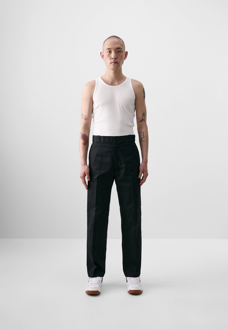 Black, tailored pants with a straight leg design, worn with a white tank top and white sneakers. Smooth fabric, minimal detailing.